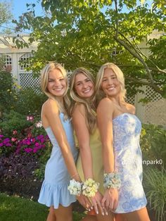 three beautiful young women standing next to each other in front of a tree and flowers