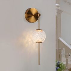 a wall mounted light on the side of a white wall next to stairs and flowers