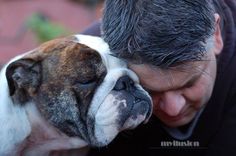 a man is hugging his dog while he looks down at the ground with his eyes closed