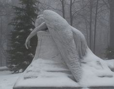 an angel statue sitting in the middle of a snow covered ground next to a pine tree