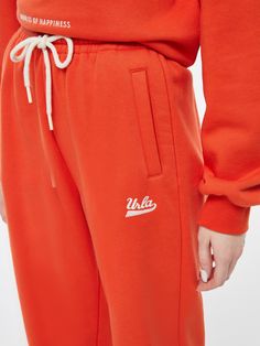 Details: Cotton fleece lounge pants in soda pop orange Elasticized waistband and cuffs Contrasting drawstring Side seam pockets Single welt pocket on back 'Urla' embroidery on front left leg Pair with "Orange Soda" Crewneck Materials & Care: 84.3% Cotton, 15.7% Polyester Hand wash | Dry clean Do not bleach Size & Fit: Model is 5'7", Bust 32, Waist 24, Hips 35, wearing a size S Item #: IL4PA33 Orange Pants With Elastic Waistband For Loungewear, Orange Drawstring Bottoms For Loungewear, Orange Cotton Sweatpants With Pockets, Orange Sweatpants With Pockets For Loungewear, Orange Bottoms With Elastic Waistband For Loungewear, Sporty Orange Bottoms With Drawstring, Orange Cotton Athleisure Bottoms, Orange Relaxed Fit Cotton Sweatpants, Sporty Orange Cotton Bottoms