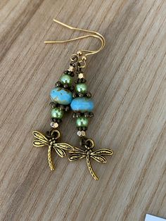 a pair of earrings with dragonflys and pearls on them sitting on a wooden surface