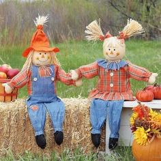 two scarecrows sitting on hay bales with pumpkins and apples in the background