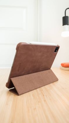 an ipad case sitting on top of a wooden table next to a lamp and phone