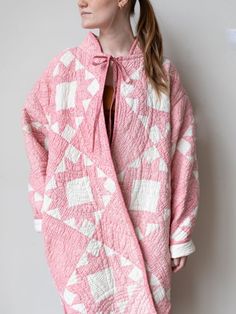 a woman standing in front of a wall wearing a pink and white quilted coat