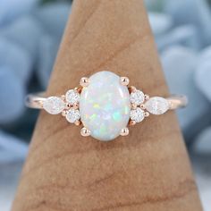 a white opal and diamond ring sitting on top of a wooden stand