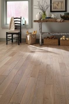 a wooden floor in a living room with chairs and pictures on the wall behind it