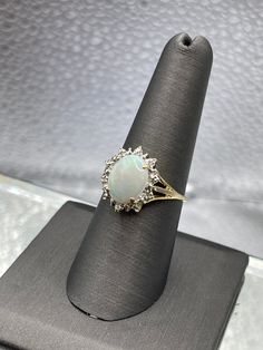 A ladies beautifully designed 14 karat solid yellow gold ring with a large oval shaped Opal accented with a halo of diamonds.   Weight:  2.9 grams Size:  8 Our Price $499.00 Regularly Priced At $850.00 Please See Our Video Remember - If you're purchasing for yourself or a gift for a loved one, buy with confidence.  We Guarantee Everything We Sell!  SKU #R961 Gold Oval Cabochon Diamond Ring For Formal Occasions, Gold Diamond Ring Oval Cabochon For Formal Occasions, Formal Gold Diamond Ring With Oval Cabochon, Oval Halo Diamond Ring For Formal Occasions, White Oval Cluster Ring For Anniversary, Oval Diamond Halo Ring For Formal Occasions, Formal Oval Diamond Ring With Halo Design, Exquisite Oval Halo Ring For Formal Occasions, Elegant Diamond Halo Ring