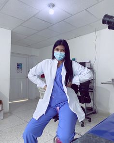 a woman in scrubs is sitting on a stool wearing a face mask and blue pants