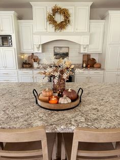 a kitchen with white cabinets and marble countertops, an island with chairs and a centerpiece that has fall decorations on it