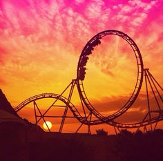 a roller coaster at sunset with the sun setting in the background and clouds above it