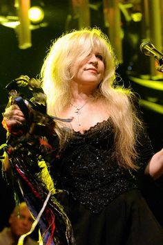 a woman with long blonde hair holding a microphone and wearing a black dress on stage