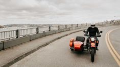 a man riding on the back of a motorcycle down a street next to a bridge