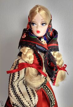 a doll with blonde hair wearing a red dress and scarf on top of it's head