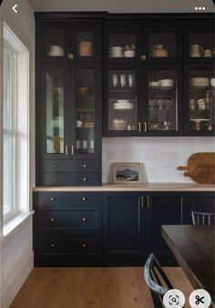 a kitchen with black cabinets and wooden floors is shown in this image, there are dishes on the shelves