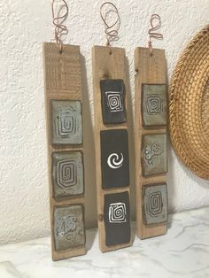 three pieces of art hanging from hooks on a wall next to a straw hat and wicker basket