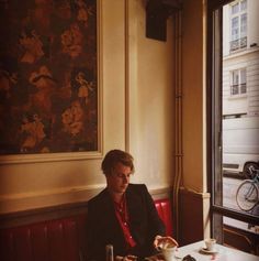 a man sitting at a table in front of a window with a cup and saucer on it