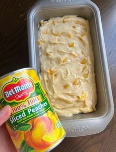 a hand holding a can of peach ice cream next to a container of sliced peaches