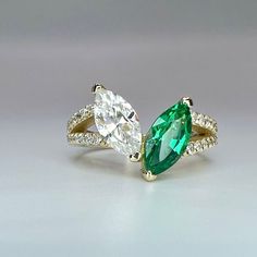 two pear shaped diamond and emerald engagement rings on a white surface with the top one in yellow gold