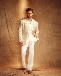 a man standing in front of a wall wearing a white suit