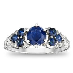 Take her breath away with this colorful vintage-inspired sapphire and diamond engagement ring. Expertly crafted in 14K white gold, the eye is drawn to the 6.0mm bright blue sapphire center stone. Trios of smaller blue sapphires flank each side of the center stone, while shimmering diamonds and intricate milgrain detailing adorn the ring's split shank. An elegant choice, designed to sparkle for a lifetime, this ring captivates with 1/8 ct. t.w. of diamonds and a polished shine. Boho Wedding Ring, Sapphire And Diamond Engagement Ring, Diamond Sapphire Engagement Ring, Split Shank Ring, Blue Sapphire Diamond, Natural Diamond Engagement Ring, Split Shank, Sapphire Stone, Diamond Stone