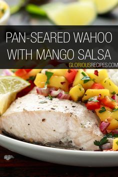 a white plate topped with fish, mango salsa and lime wedges on top of a wooden table