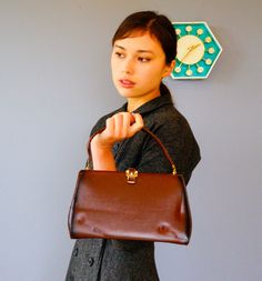 "DESCRIPTION * Vintage purse from 1950s-1960s * frame style: metal hinged frame with an opening on top, flat bottom, single handle, lift up clasp * made with faux leather * in brown color with gradient darker brown along the edge * embellished with a belt buckle clasp * lined with black fabric * interior has one small pocket * no tag CONDITION * in good vintage condition with minimal scuff marks on the leather and minimal tarnish on the goldtone hardware. Show normal signs of use. * Sold as-is. Vintage Brown Office Bag, Retro Brown Formal Bags, Vintage Brown Retro Satchel For Daily Use, Retro Satchel With Detachable Handle For Formal Use, Retro Vintage Brown Satchel For Daily Use, Retro Formal Satchel With Detachable Handle, Vintage Brown Retro Satchel Bag, Vintage Brown Retro Bag For Formal Occasions, Vintage Leather Satchel Backpack