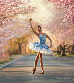 a woman in a blue and white dress is dancing on the street with cherry trees