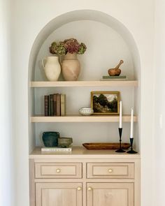 a shelf with books and vases on top of it in the corner of a room