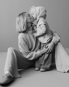 a woman sitting on the floor with her baby in her lap and kissing her cheek