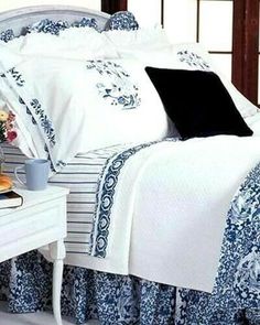 a bed with blue and white comforters on top of it next to a night stand