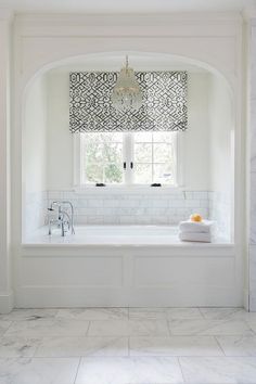 a white bathroom with marble floors and walls, along with a chandelier that hangs from the ceiling