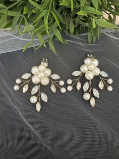 two pairs of earrings with pearls and leaves on top of a veiled table cloth