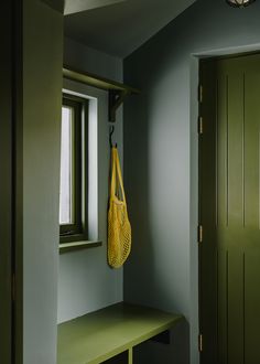 a green bench with a yellow bag hanging from it's side in front of a window