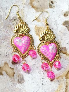 Beautiful and modern hand painted sacred heart earrings, in fuchsia pink, with pink light and silver flowers, adorned with pink glass stones. These earrings are painted in detail and look really beautiful, they are finished with high quality jewelry varnish to protect the paint. These hand painted sacred heart earrings are unique and very beautiful, the ideal gift because they match any outfit both day and night, they will enhance your beauty and you will surely attract attention due to the unique and handcrafted design, the ideal gift for holidays or simply to make that special person happy. Features/ Product info Note: The earrings in stock have some differences because they are hand painted. -The Main Material: Brass -Color: Fuchsia pink -Small: 1 in  (Please see the photos, this design Bohemian Pink Earrings With Heart Beads, Handmade Heart-shaped Earrings For Festive Occasions, Handmade Heart-shaped Festive Earrings, Pink Hand Painted Heart Jewelry, Pink Bohemian Hand Painted Jewelry, Bohemian Heart-shaped Party Earrings, Handmade Pink Jewelry For Halloween, Bohemian Pink Hand Painted Earrings, Handmade Bohemian Earrings For Halloween