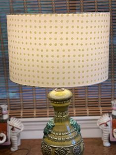 a green lamp sitting on top of a wooden table next to a window with blinds