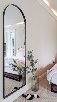 a bedroom with a bed, mirror and plant on the floor in front of it