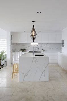 a kitchen with marble counter tops and white chairs in front of an island that has a light hanging over it