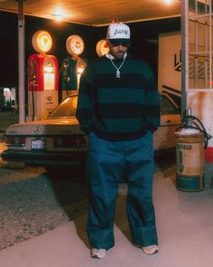 a man standing in front of a gas station with his hand on his hip and wearing a hat