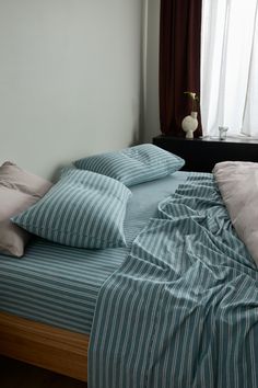 an unmade bed with blue and white striped sheets