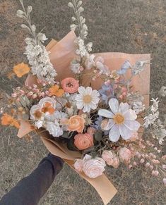 a person holding a bouquet of flowers in their hand on top of some grass and dirt