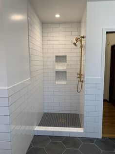 a walk in shower sitting next to a white tiled wall and floor covered in gray tile