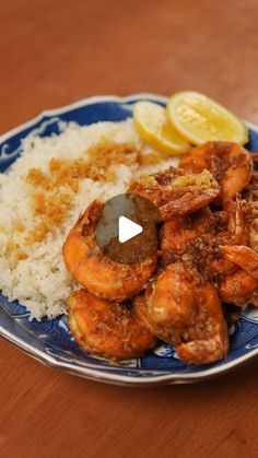 a blue and white plate topped with rice covered in shrimp next to lemon wedges