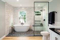 a white bath tub sitting under a window next to a toilet in a room with wooden floors