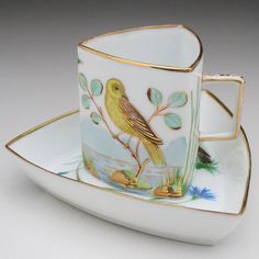 a cup and saucer with a bird painted on the side sitting on a plate