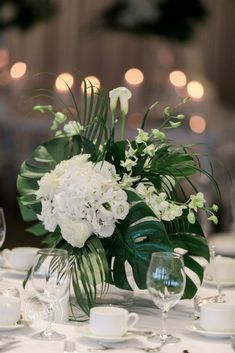 a vase filled with white flowers sitting on top of a table next to wine glasses