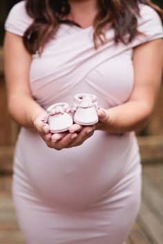 a pregnant woman holding baby shoes in her hands