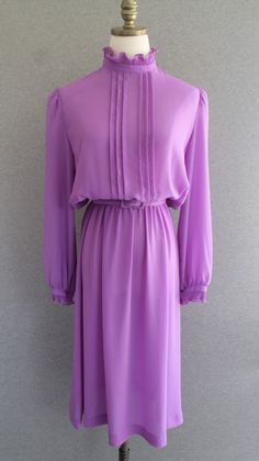 "This lilac dress features pin-tuck pleats down the front of the bodice to the elastic waist.   There are ruffles at the neck and cuff.   The belt is of the same fabric with the belt buckle being very slightly bent.  The belt is marked \"size 16\", but we thinks the size is more of a 10/12.  Check measurements. Estimated size 10/12 40\" bust 22-32\" waist 50\" total hip 44\" nape to hem  Purveyor's Note: We have searched far and wide, wrestled bears, braved the cold, traversed mountain ranges, f Elegant Purple Pleated Dress, Formal Purple Dress With Pleated Bodice, Elegant Mauve Daywear Dress, Elegant Mauve Dress For Daywear, Purple Pleated Wedding Dress, Party Dress Wedding, Taco Stand, Lilac Lavender, Mountain Ranges