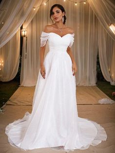 a woman standing in front of a white backdrop wearing a wedding dress with off the shoulder sleeves