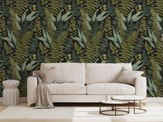 a white couch sitting in front of a wall with green leafy designs on it